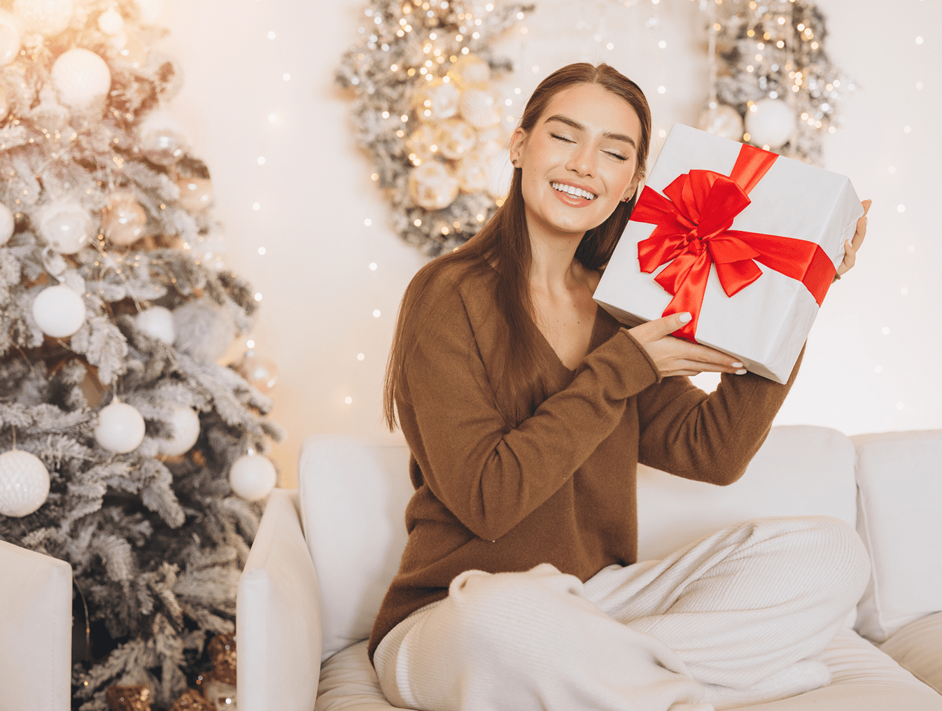 Woman holding gift by Christmas tree