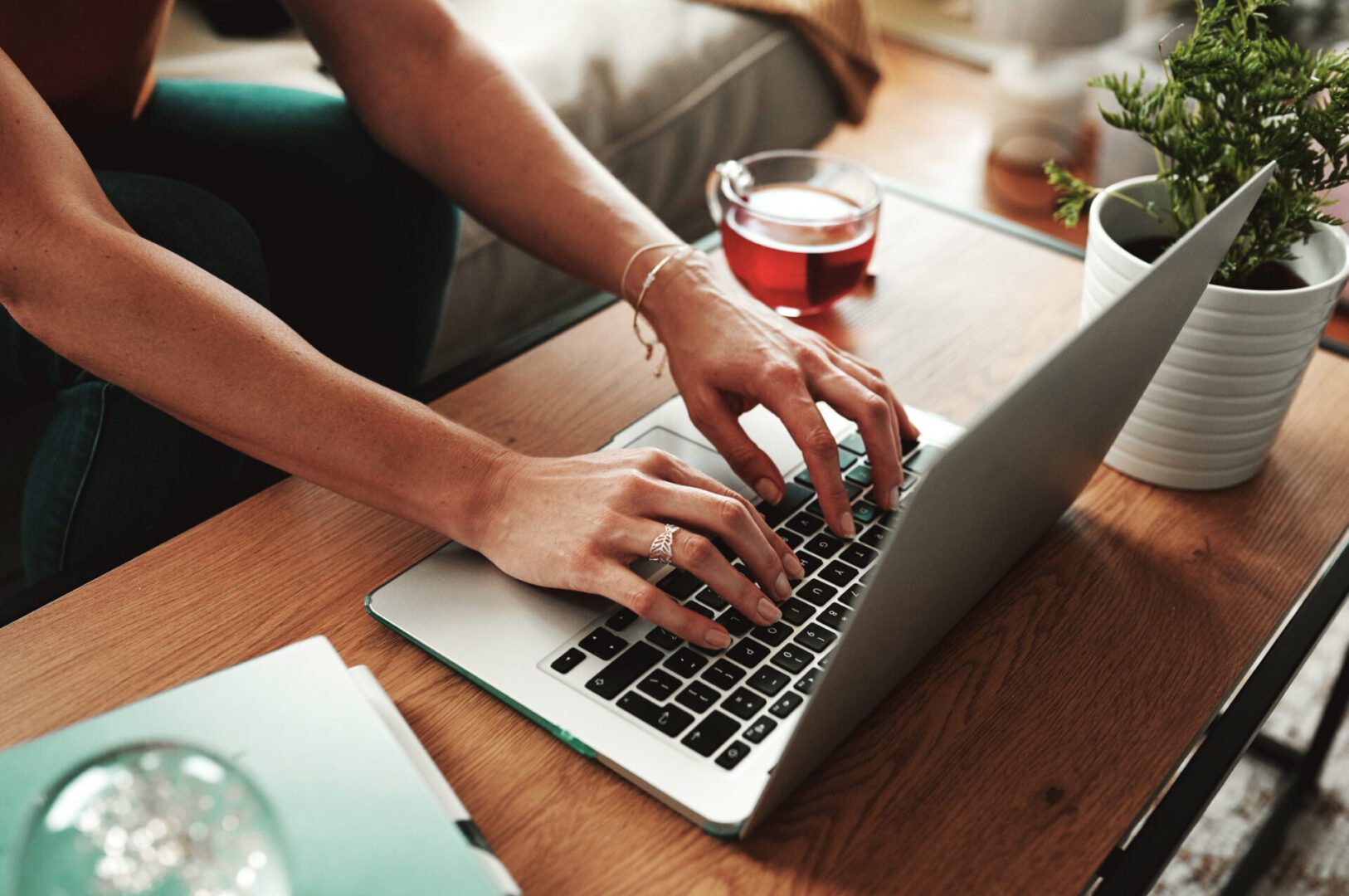 Hands typing on a laptop, cup nearby.