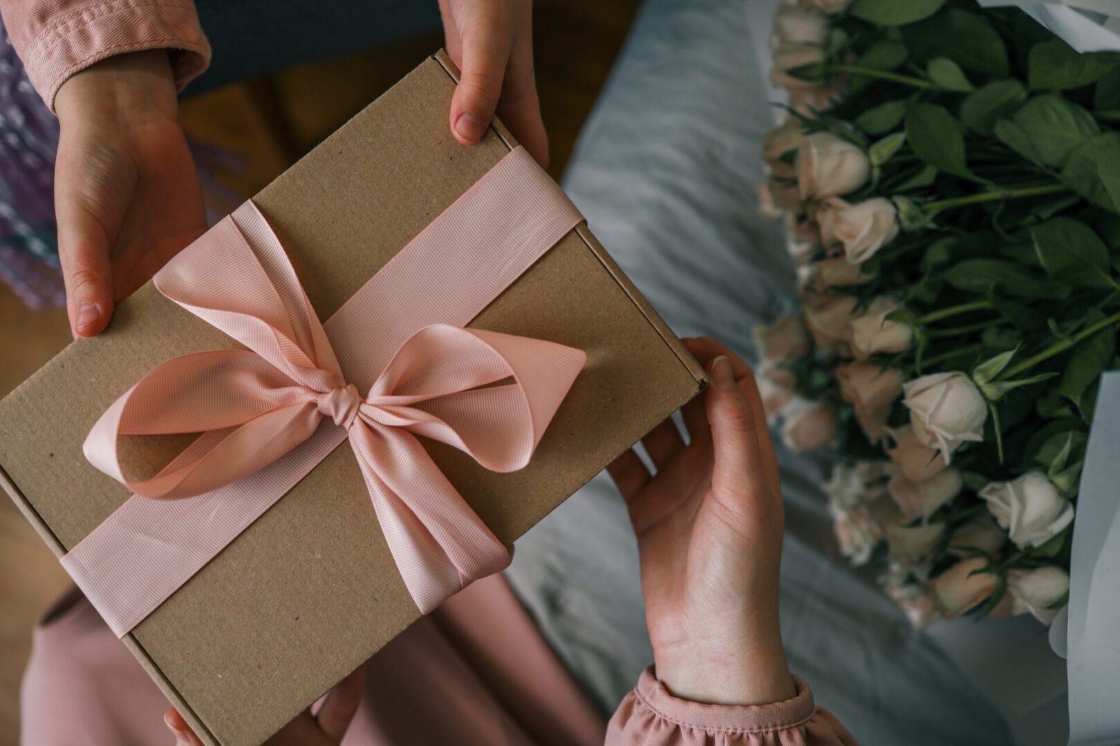 Gift box with pink ribbon, flowers nearby.