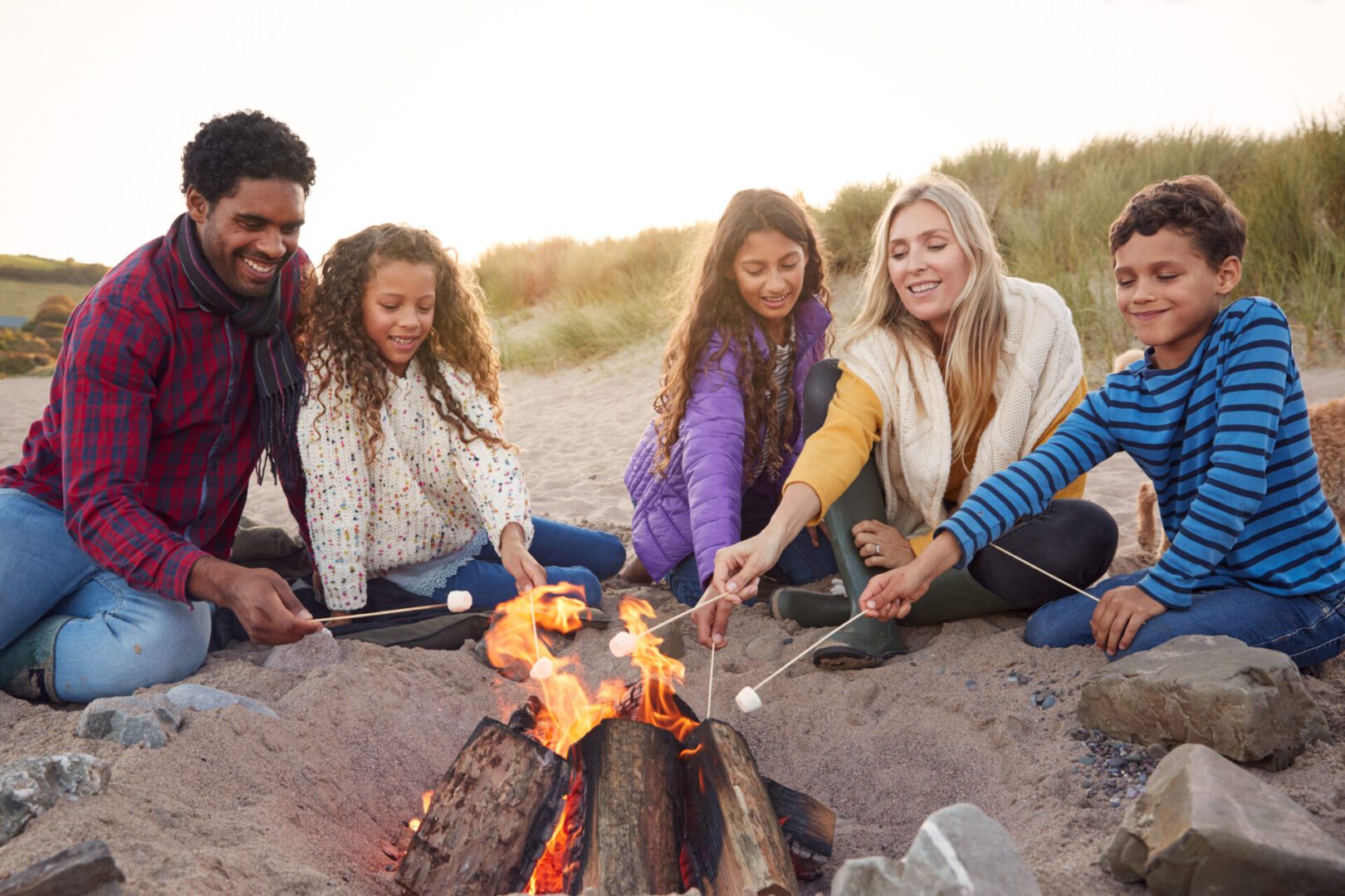 Family roasting marshmallows around beach campfire.