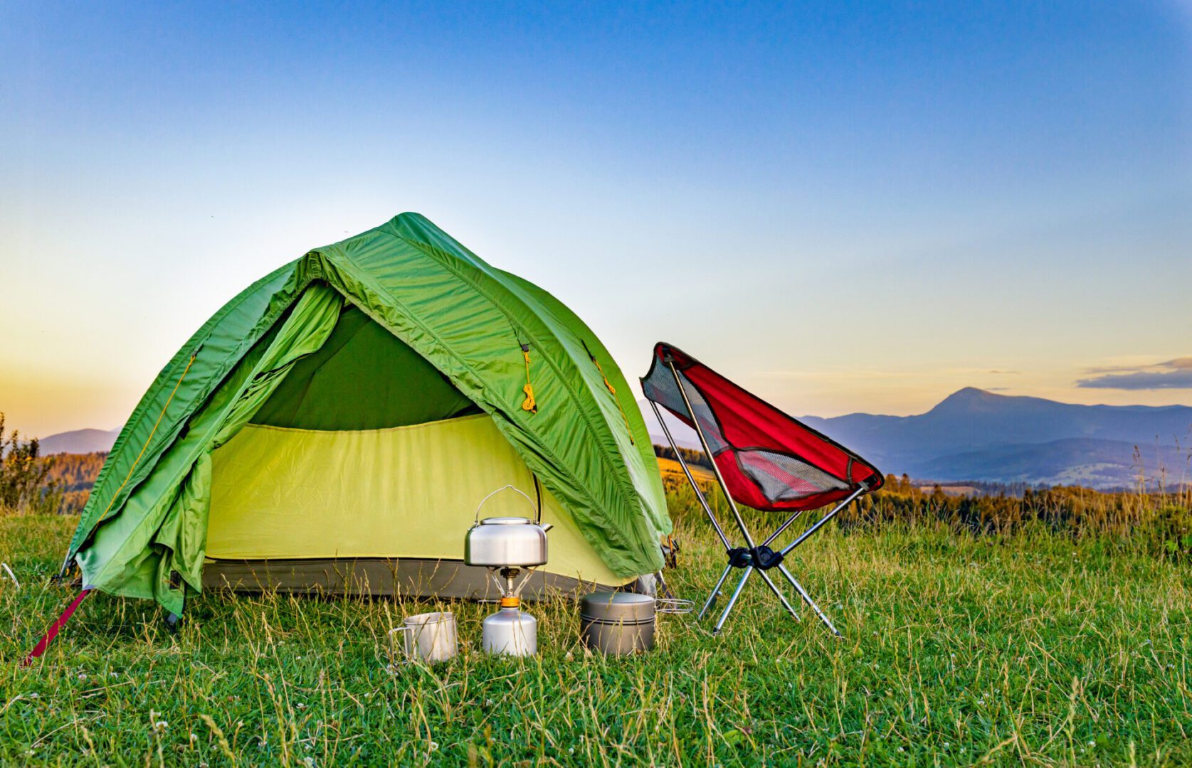 Green tent and chair on grassy field.