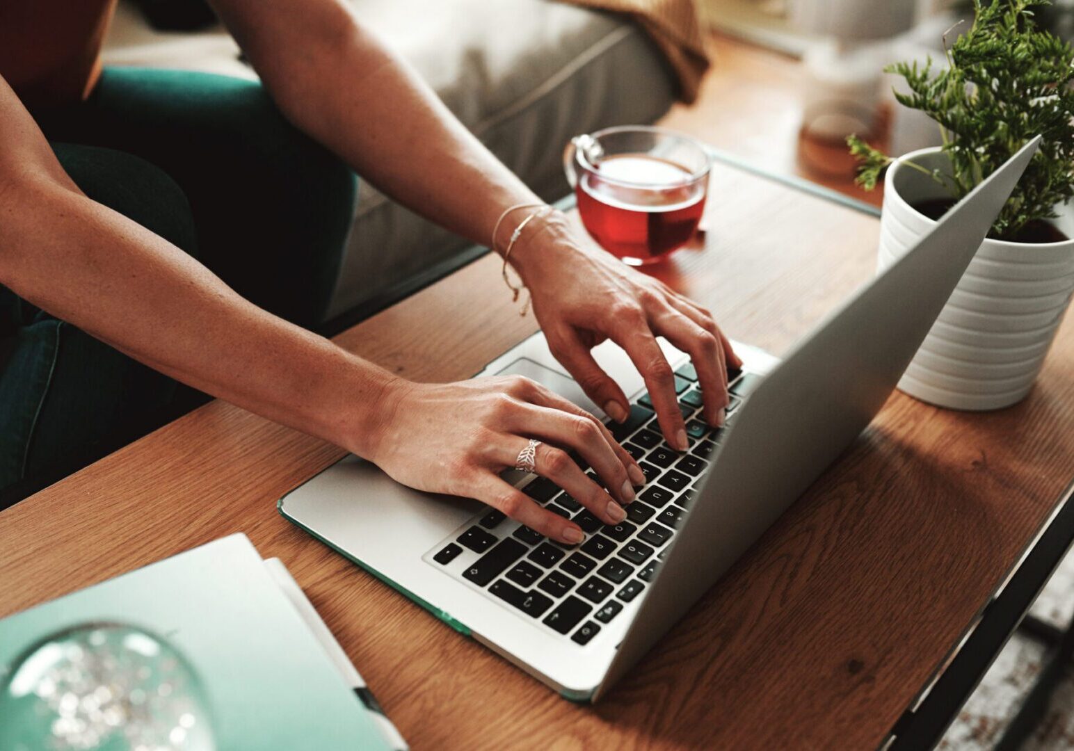 Hands typing on a laptop, cup nearby.