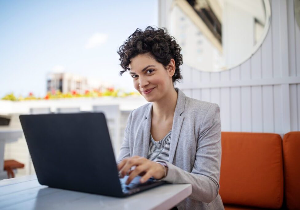 Woman smiling while using a laptop outdoors.