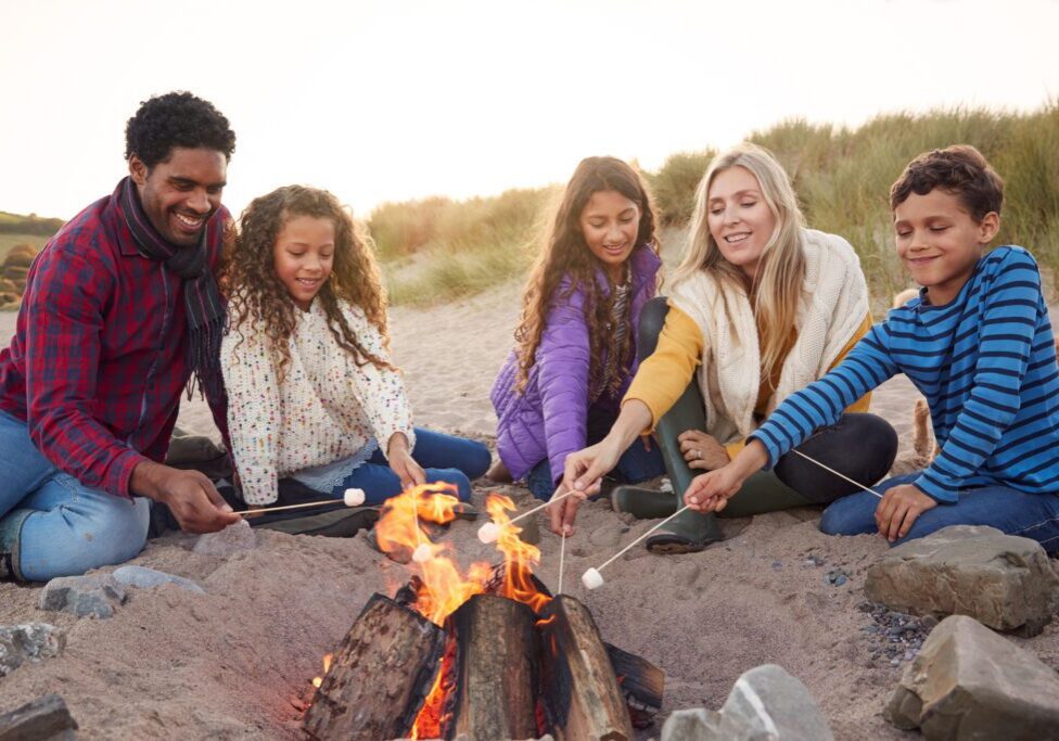 Family roasting marshmallows around beach campfire.