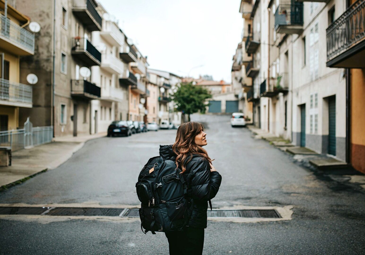 Traveler with backpack walking down urban street.