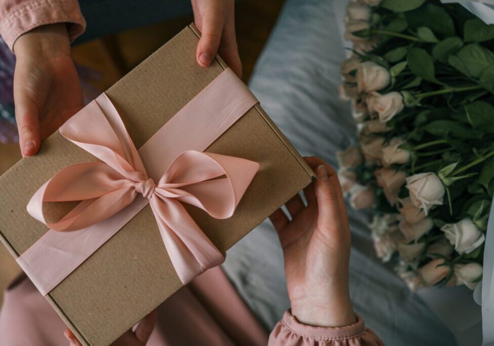 Gift box with pink ribbon, flowers nearby.