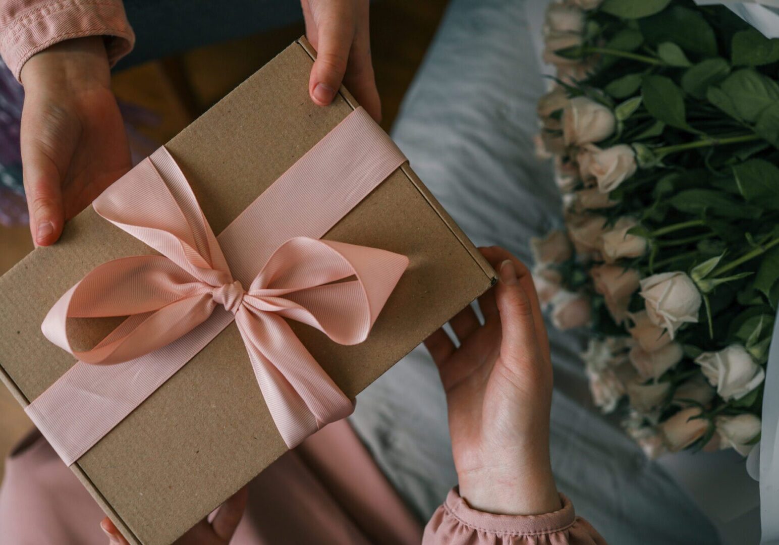 Gift box with pink ribbon, flowers nearby.